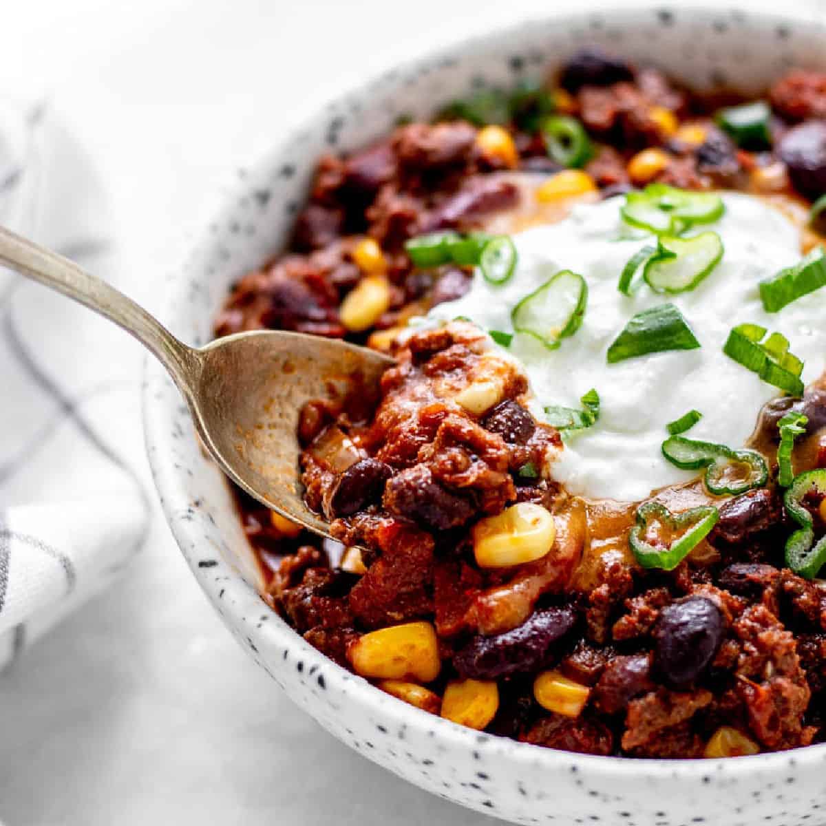 A bowl of chili con carne with a dollop of sour cream and a spoon.
